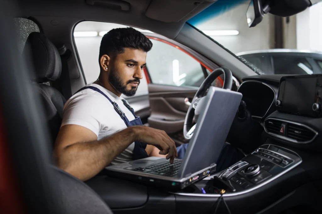 Mechanic using diagnostics laptop inside a modern car